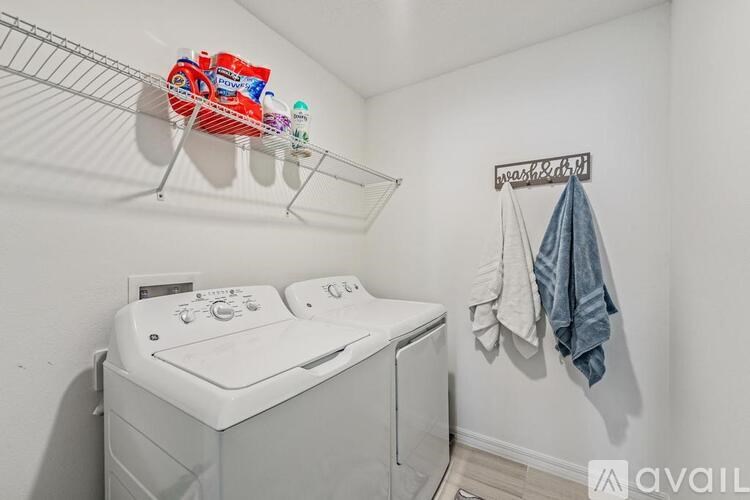 A white washing machine sits in a small laundry room with a clothes drying rack above it.