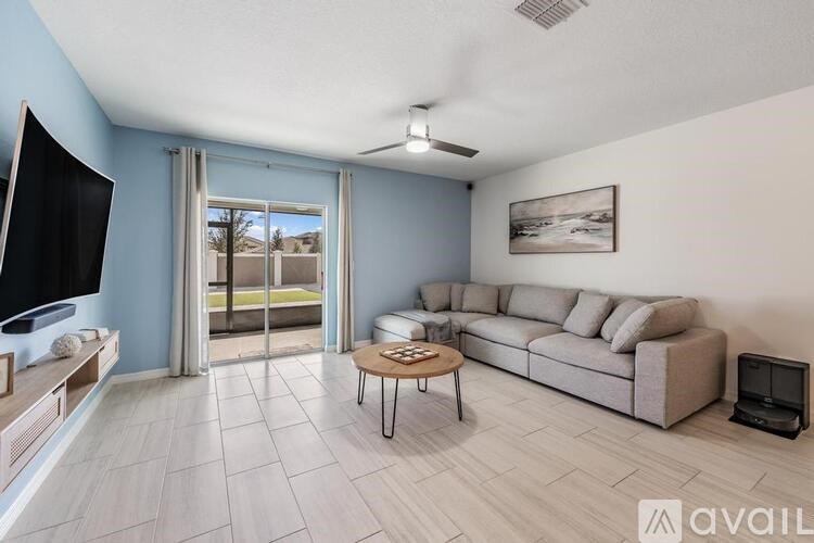 A living room with a grey couch, a television, a coffee table, and a window with a view of the outdoors.