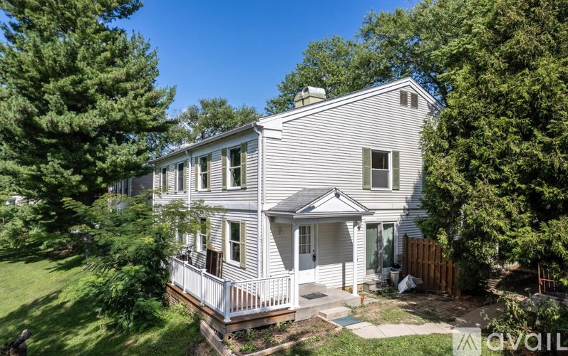 A house with a white exterior and a balcony is surrounded by greenery.