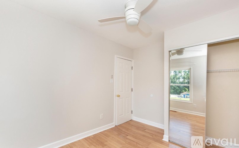 A room with a white door and a window with a view of trees.