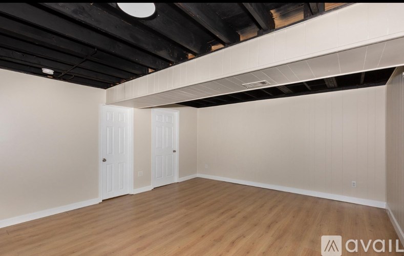 A room with wooden flooring and white walls, with a ceiling that has exposed beams.