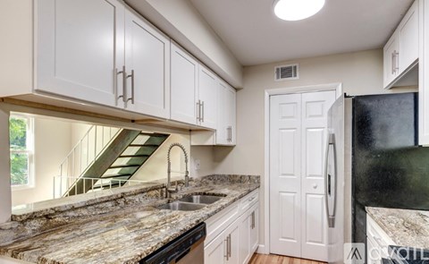 A kitchen with a granite countertop and a black refrigerator.