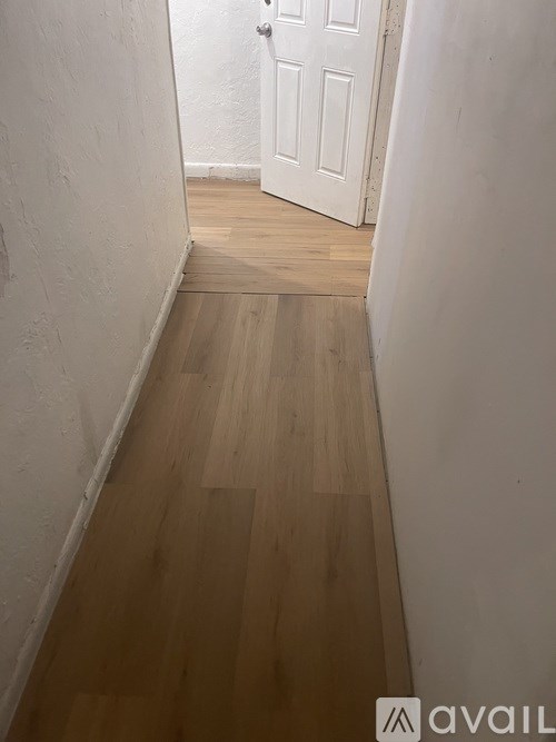 A hallway with a white door and wooden flooring.