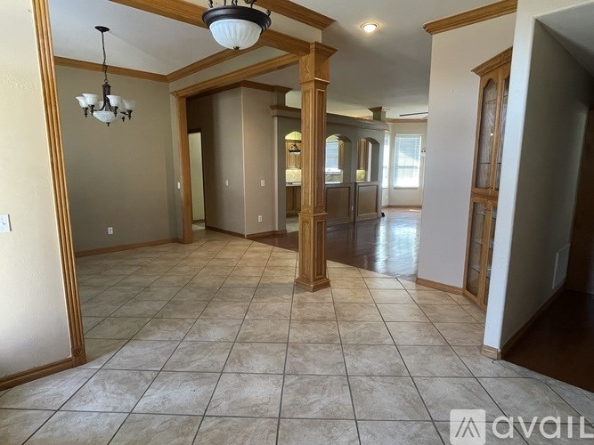 A spacious living room with a chandelier and a kitchen in the background.