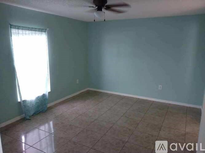A room with a ceiling fan and a window with curtains.
