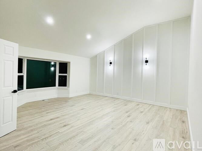 A room with white walls and wooden flooring with a door on the left side.