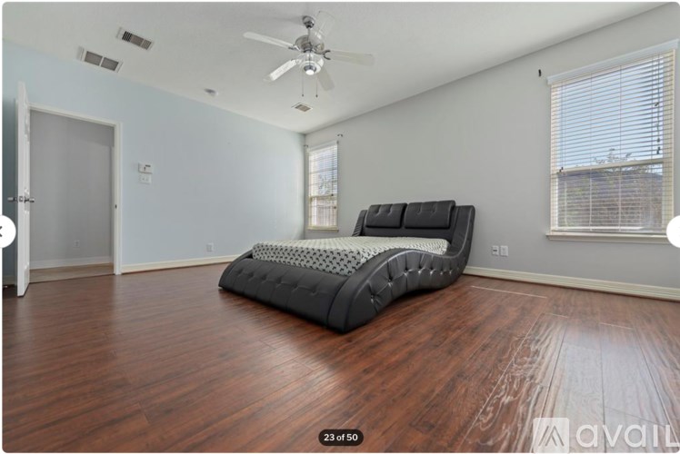 A large bed with a black headboard is in a room with wooden floors and a ceiling fan.
