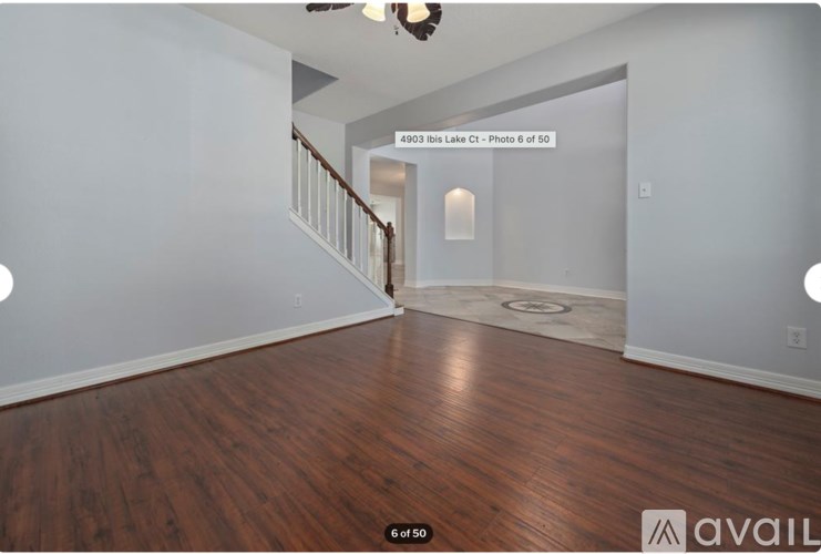 A living room with wood flooring and a staircase in the background.