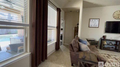 A living room with a couch, a television, and a window with blinds.