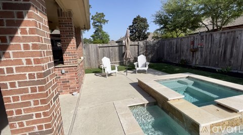 A small pool in a backyard with a patio and two chairs.