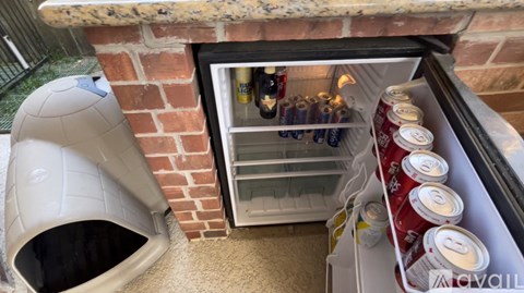 A small refrigerator is filled with canned goods and is located under a counter.