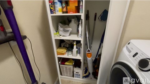 A white shelf with cleaning supplies and a vacuum cleaner on the floor.