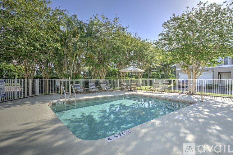 A pool surrounded by trees and a fence with chairs around it.