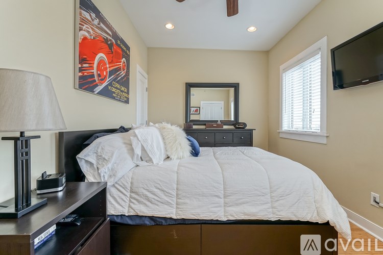 A bedroom with a large bed, a lamp, and a painting of a red car on the wall.