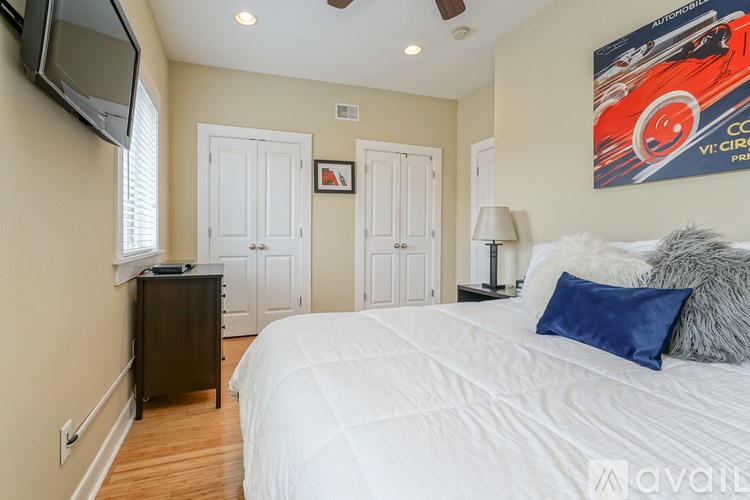 A bedroom with a large bed and a painting of a red car on the wall.