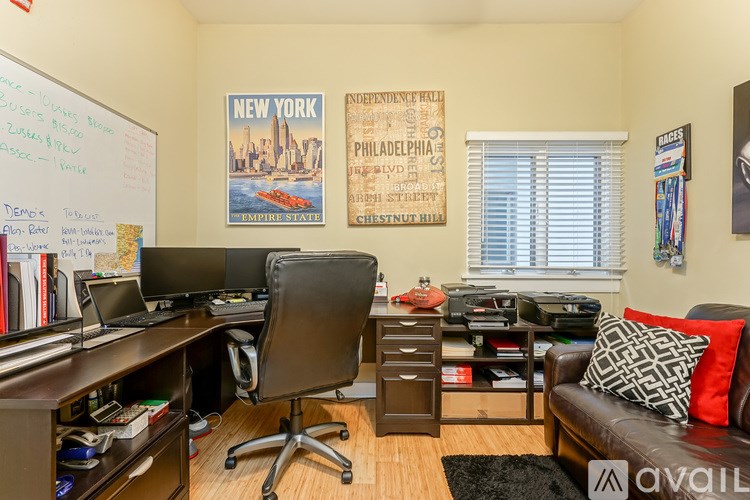 A room with a whiteboard, a desk with a computer, a chair, and a couch with a pillow.