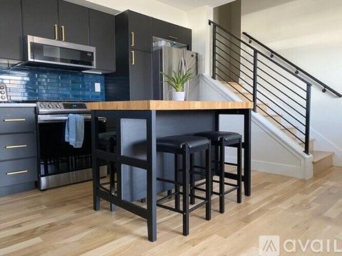 A kitchen with black cabinets and a wooden island with two stools.