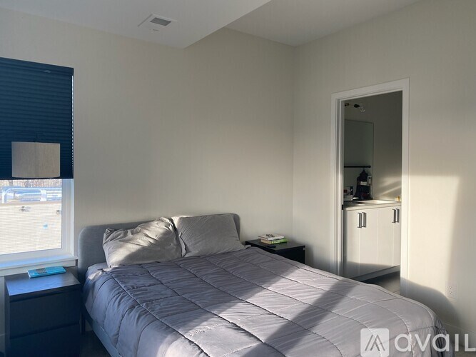 A bedroom with a bed, nightstand, and a window with blinds.