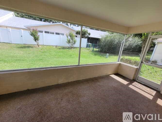 A room with a carpeted floor and a view of a white fence and greenery outside.