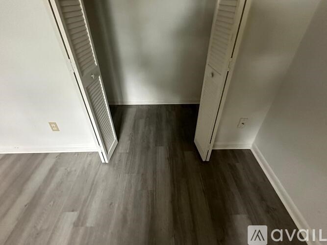 A room with a wooden floor and a white wall with a door on the right side.