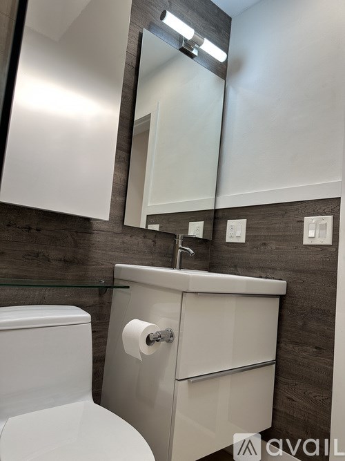 A bathroom with a toilet, sink, mirror, and wooden wall paneling.