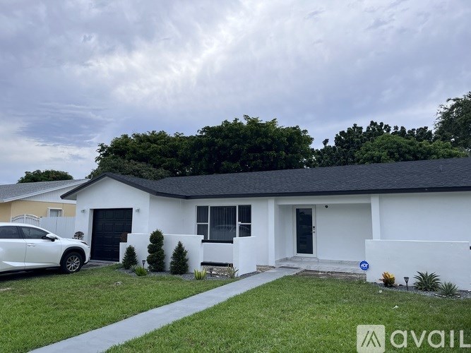 A white house with a car parked in front and a blue sign on the lawn.