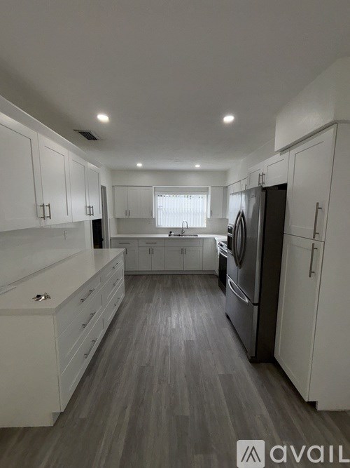 A modern kitchen with white cabinets and a wooden floor.