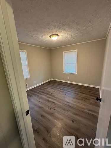 A room with wooden flooring and two windows.