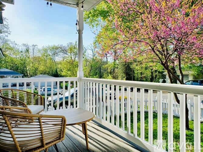 A wooden chair and table are on a white railing with a tree in the background.