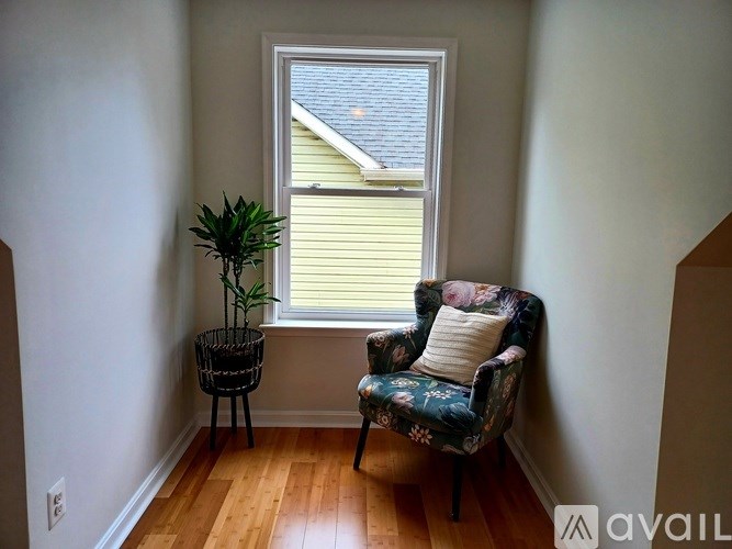 A chair with a floral pattern sits in front of a window with a plant beside it.