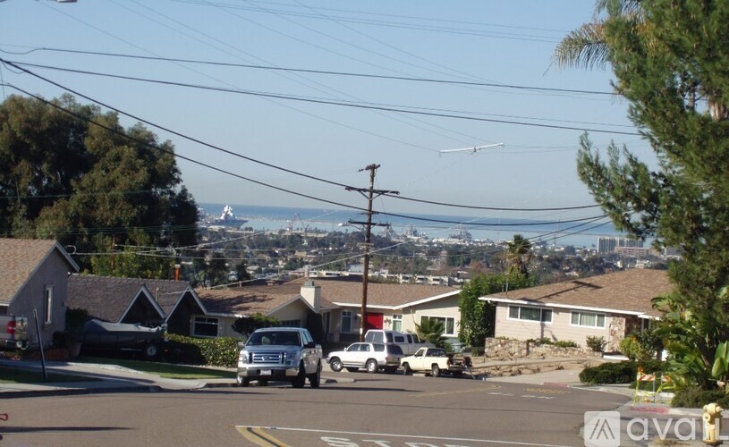 A suburban street with cars parked on the side and houses in the background.