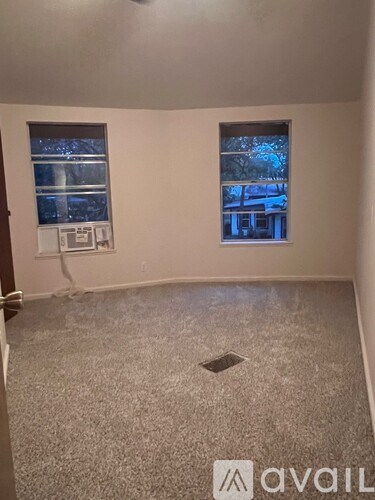 A room with a carpeted floor and two windows.