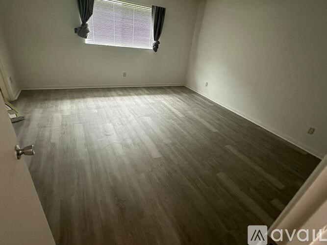 A room with wooden flooring and a window with curtains.