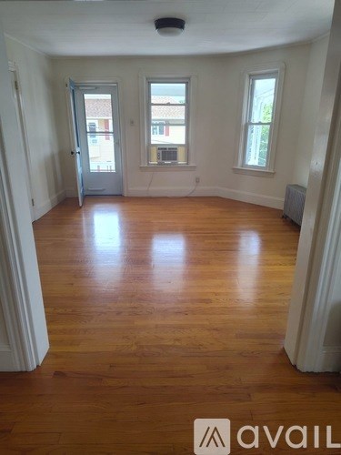 A room with wooden floors and white walls, with a door and two windows.