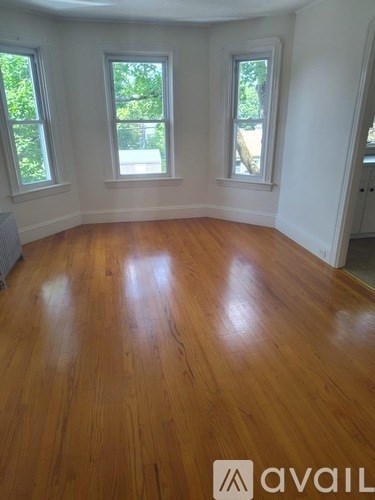 A room with wooden flooring and three windows.