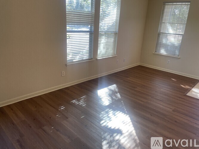 A room with wooden flooring and two windows with blinds.