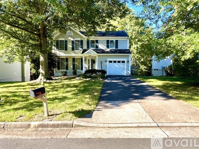 A two-story house with a white garage door is surrounded by greenery.