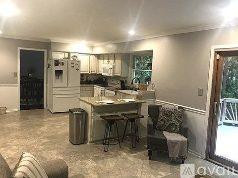 A kitchen with a refrigerator, sink, and a chair with a pillow on it.