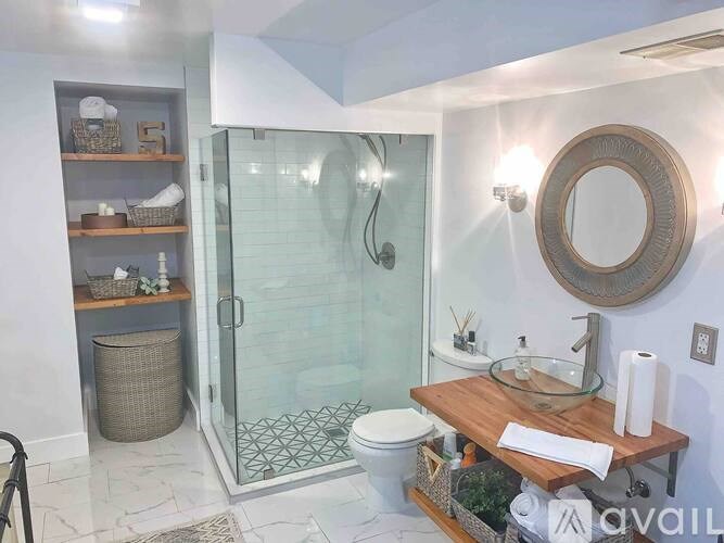 A bathroom with a glass shower door and a round mirror above the sink.