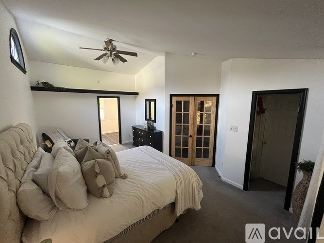 A bedroom with a bed, a ceiling fan, and a door leading to another room.