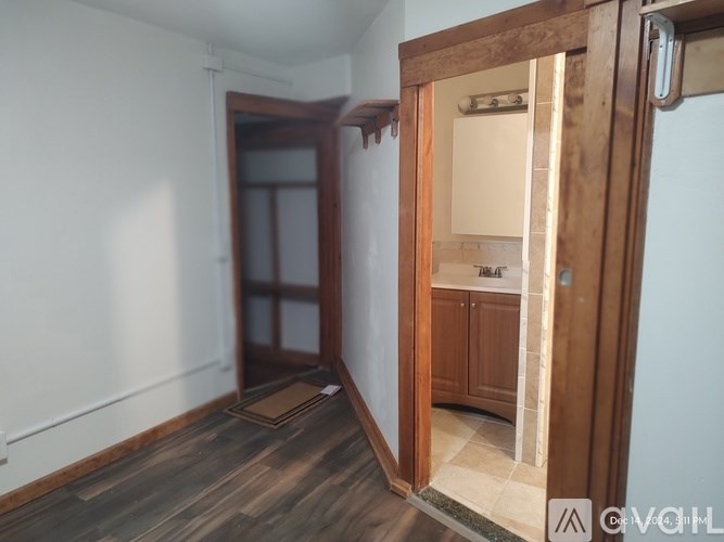 A room with a wooden floor and a white wall with a doorway leading to another room.
