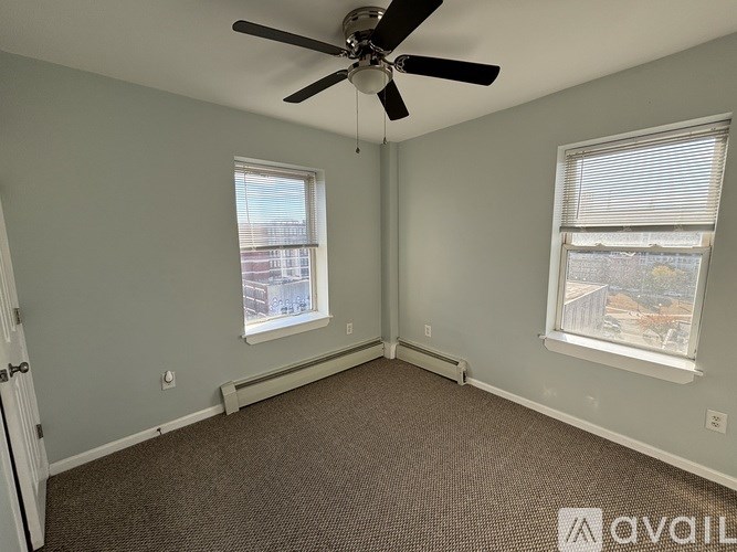 A room with a ceiling fan and two windows.