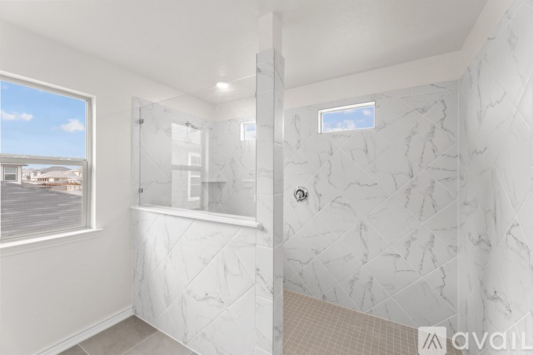 A bathroom with a marble patterned shower and a window overlooking a parking lot.