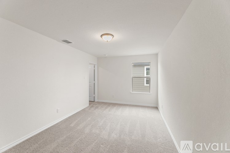 A spacious, empty room with a carpeted floor and a window with blinds.
