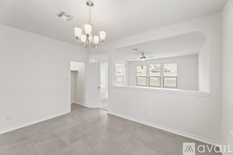 A spacious living room with a chandelier, ceiling fan, and large windows.