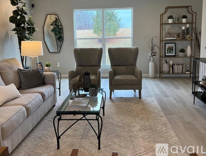 A living room with two chairs, a sofa, a coffee table, and a shelf with various decorative items.