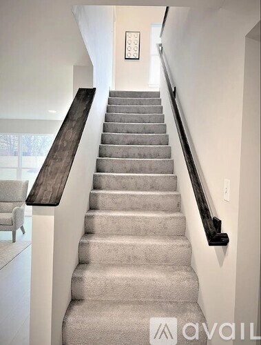 A staircase with a wooden handrail and beige carpeted steps.