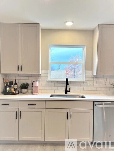 A kitchen with white cabinets and a window showing trees outside.