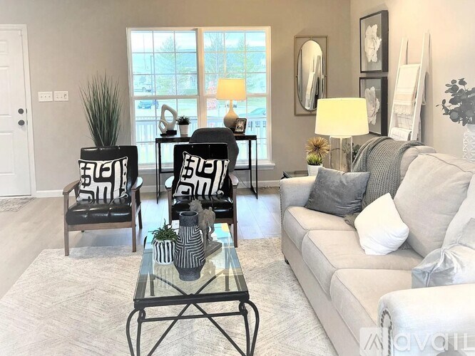 A living room with a grey couch, a glass coffee table, and two chairs with black and white cushions.
