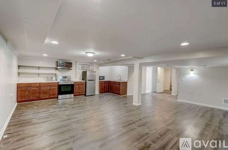 A spacious living room with wooden flooring and a kitchen area in the background.